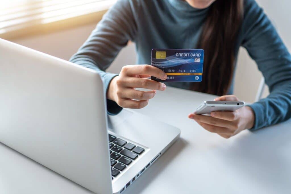 Person holding a credit card while typing on a laptop keyboard
