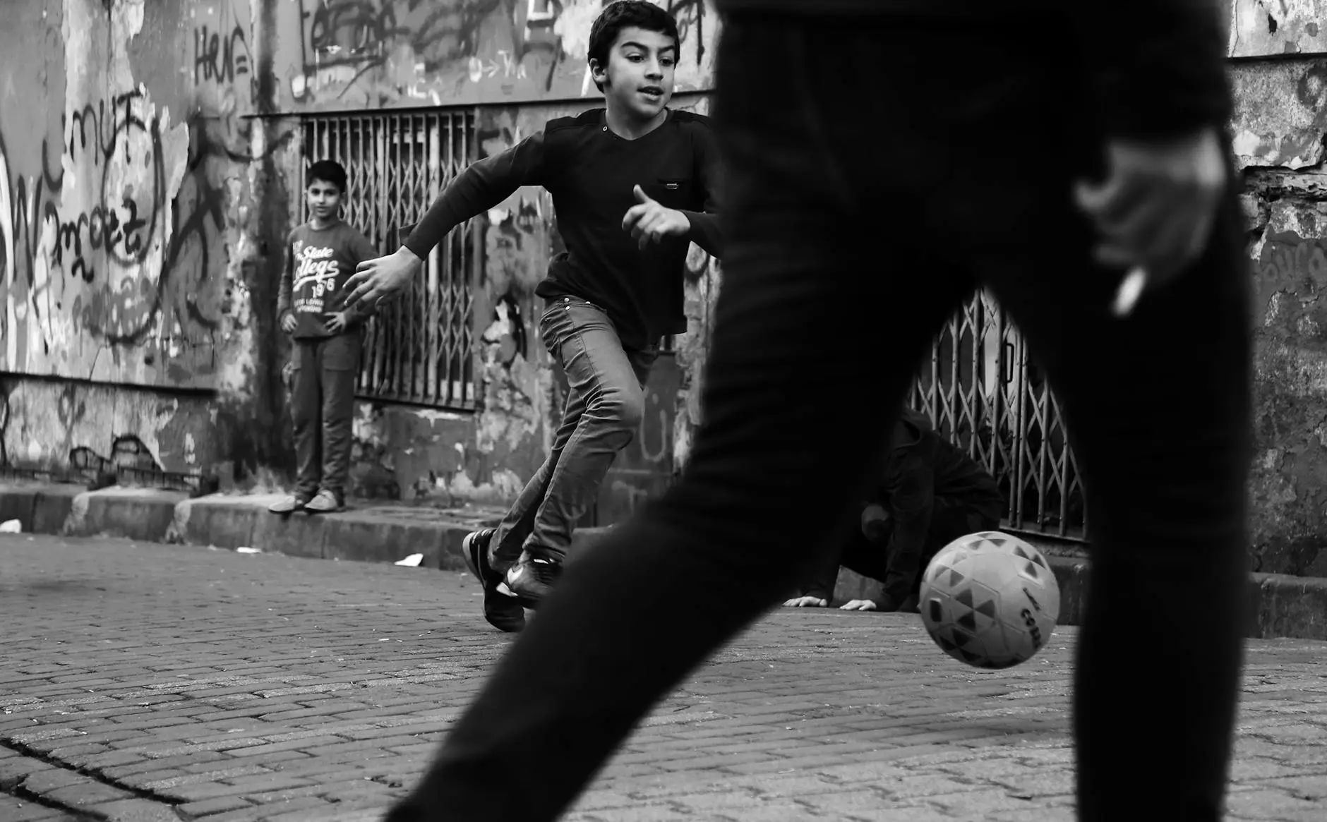 Kids playing street football in a graffiti-covered urban area.