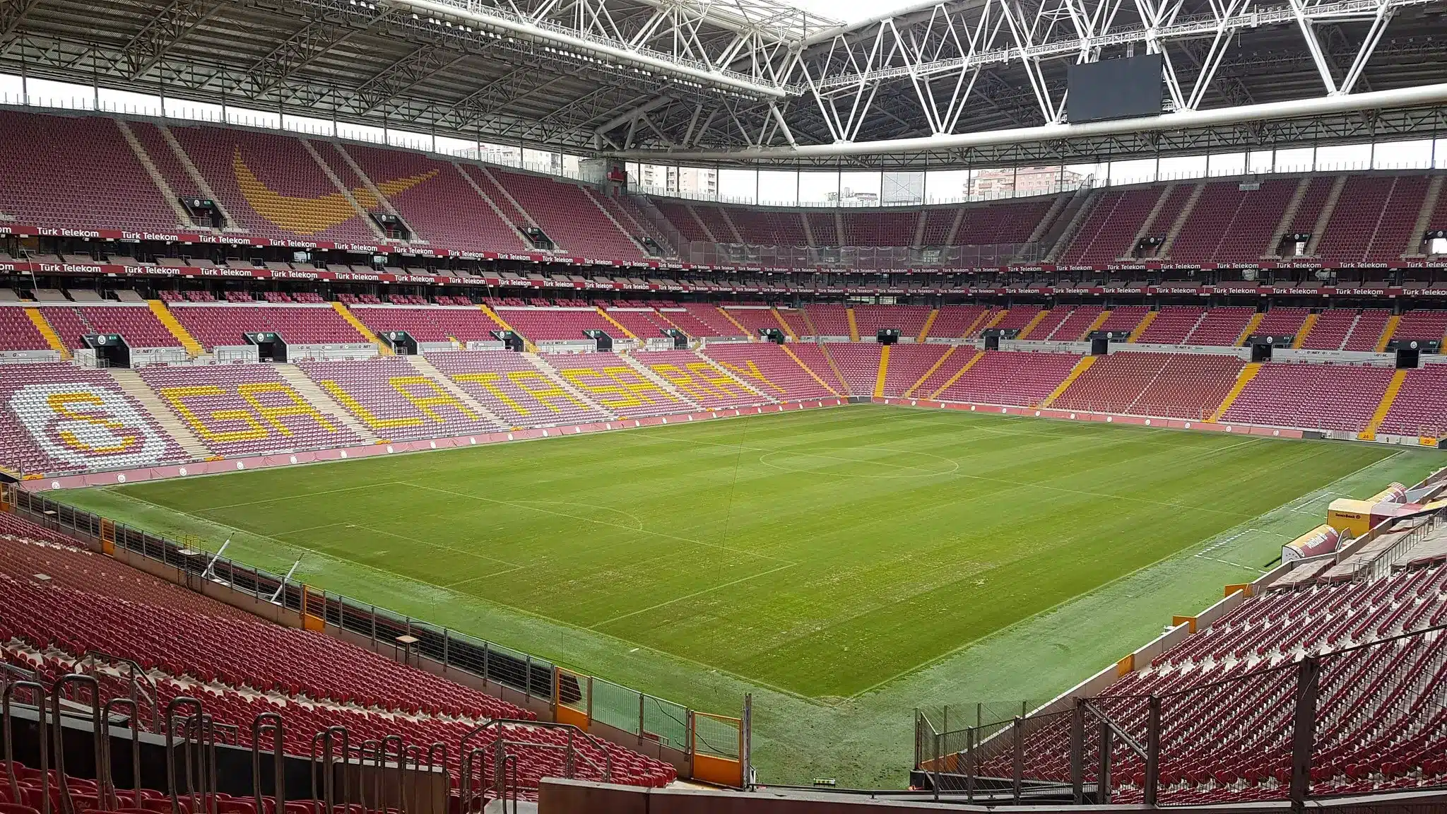 Interior view of Galatasaray RAMS Park stadium with empty seats and green pitch.