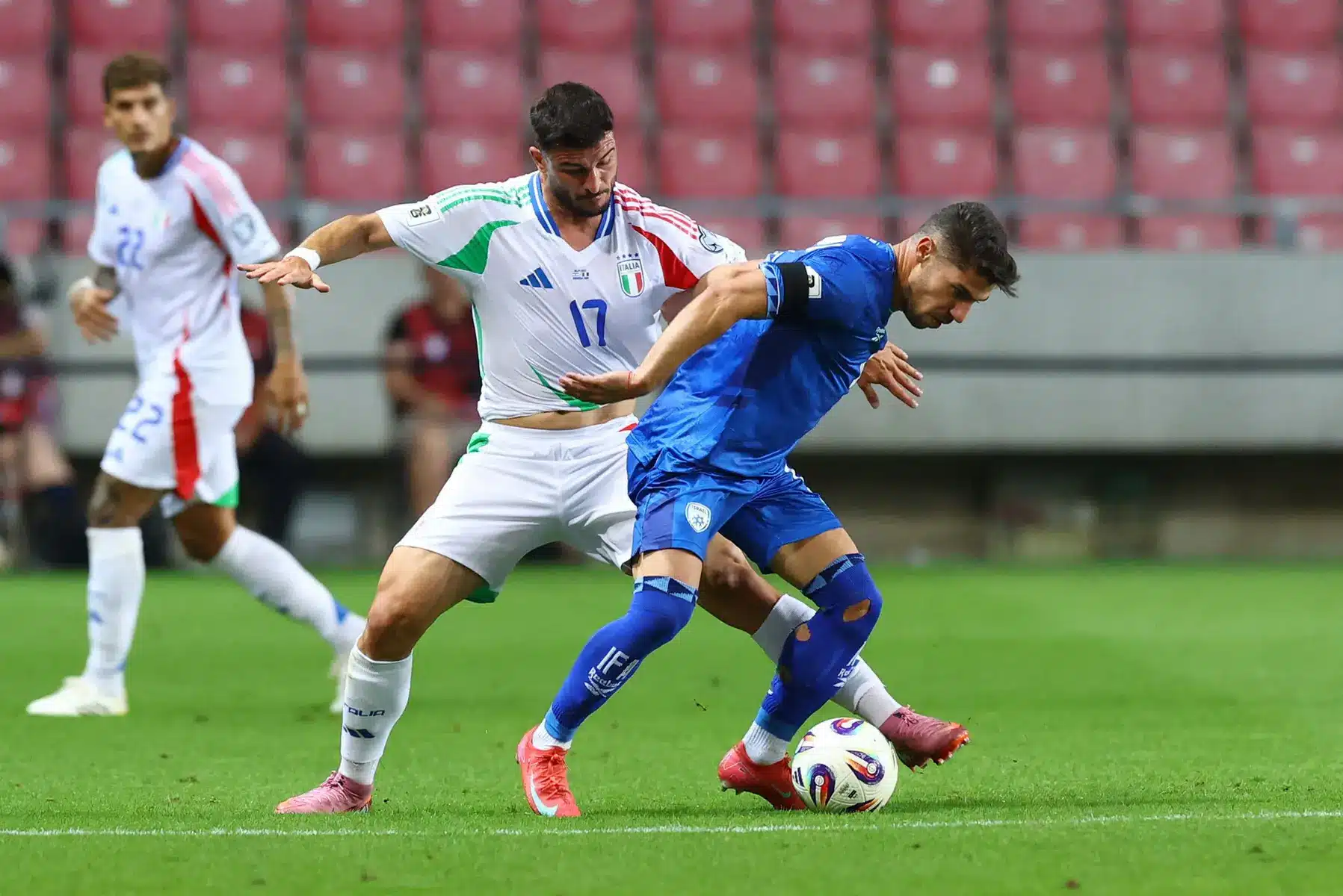 An Italy national football team player in a white kit battling for the ball against an opponent in blue.
