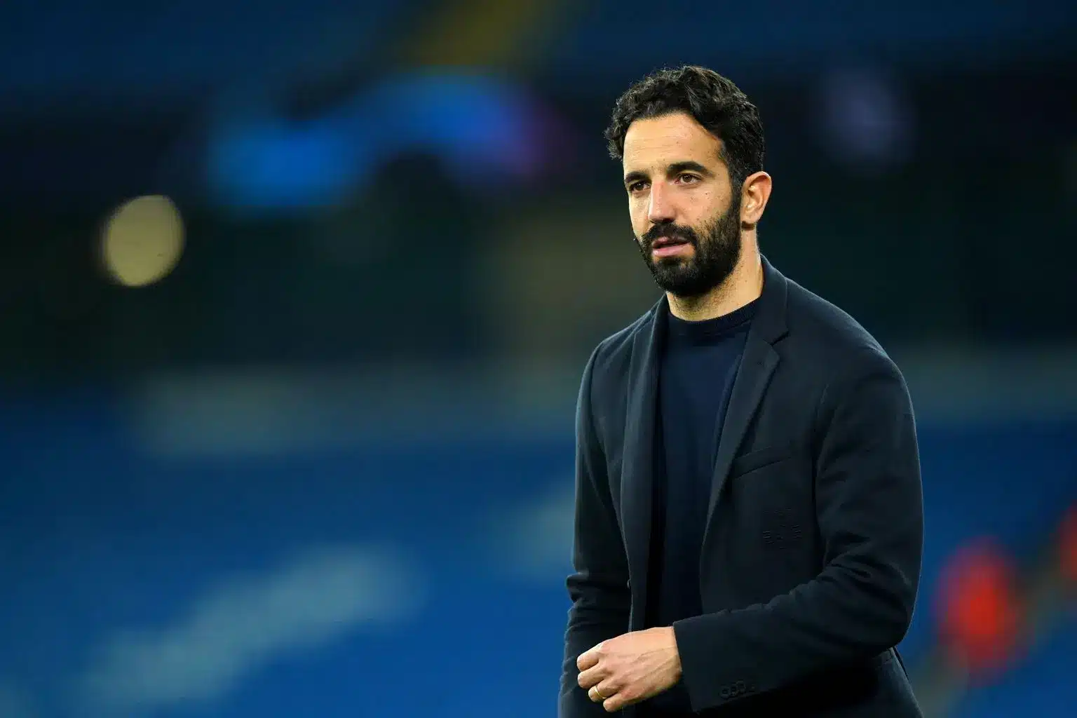 Portrait of Ruben Amorim wearing a dark navy blazer and t-shirt on a football pitch