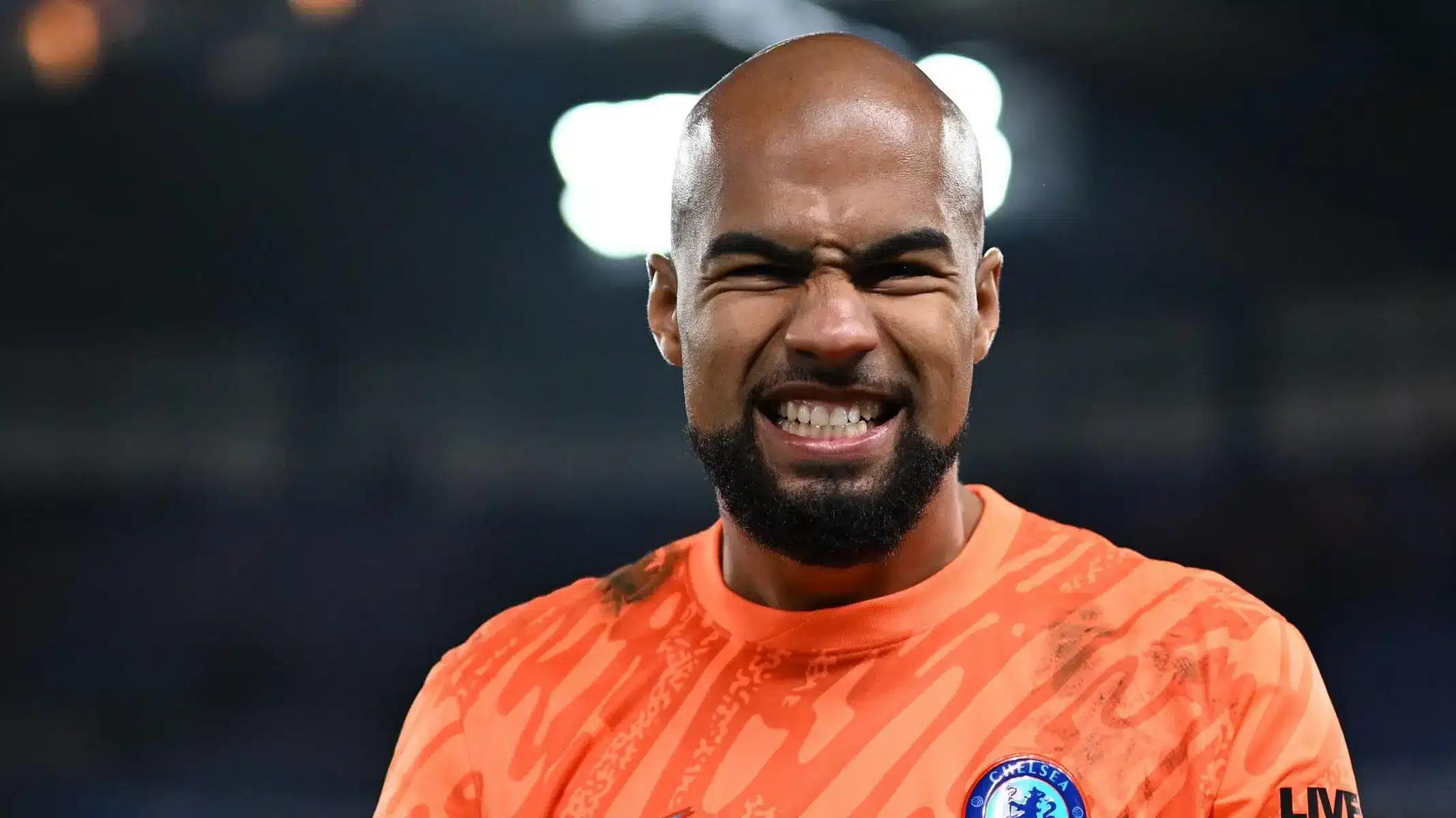 Robert Sanchez, Chelsea goalkeeper, wearing an orange jersey and making a grimacing facial expression.